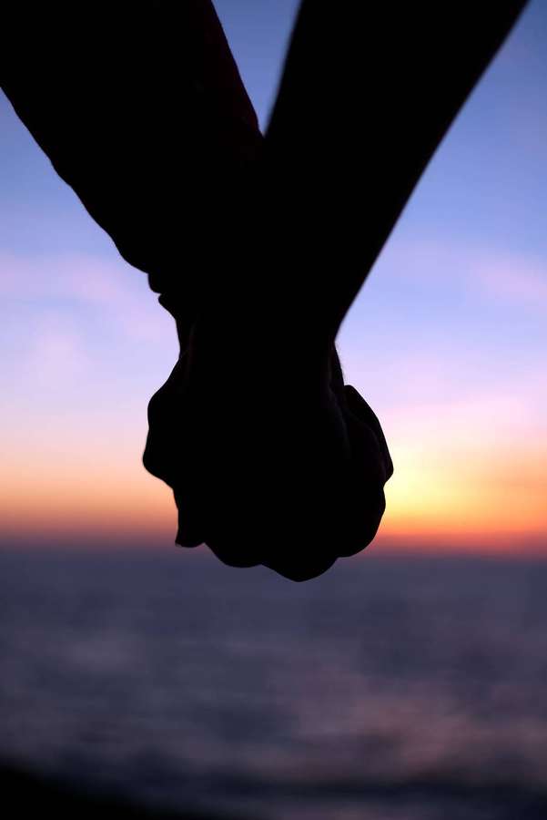 Zwei Hände, die fest gegen einen Sonnenuntergang über dem Ozean halten. — Hand In Hand Bilder