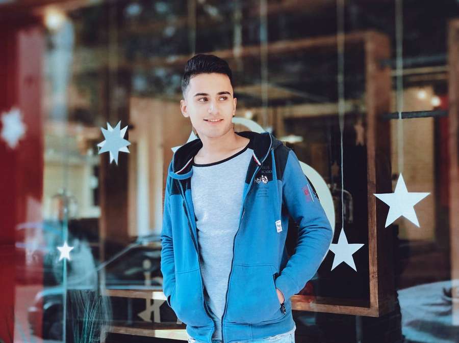 Young man in blue hoodie smiling outside glass store with star decorations. — Handsome Boy Wallpaper