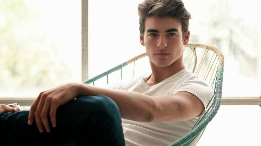 Young man sitting in a chair by a window wearing casual clothes. — Handsome Man Wallpaper