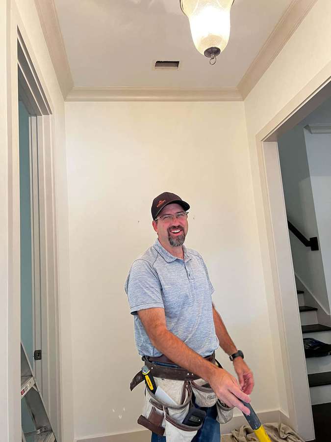 A cheerful handyman holding a paint roller in a newly painted hallway. — Handyman Wallpaper