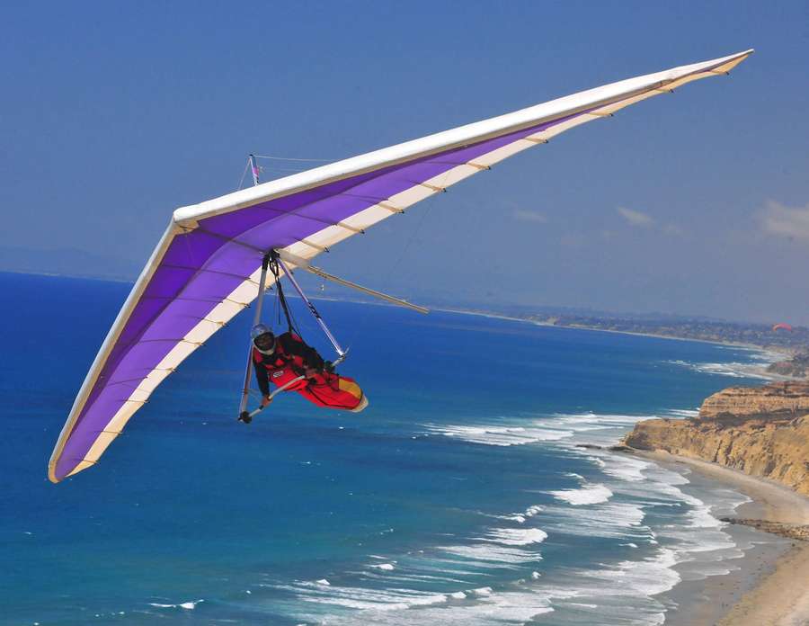 Hang glider flying over ocean coastline on sunny day — Hang Gliding Wallpaper