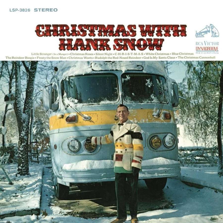 Hank Snow in festive coat standing beside snow-covered vintage bus in winter scene. — Hank Snow Wallpaper