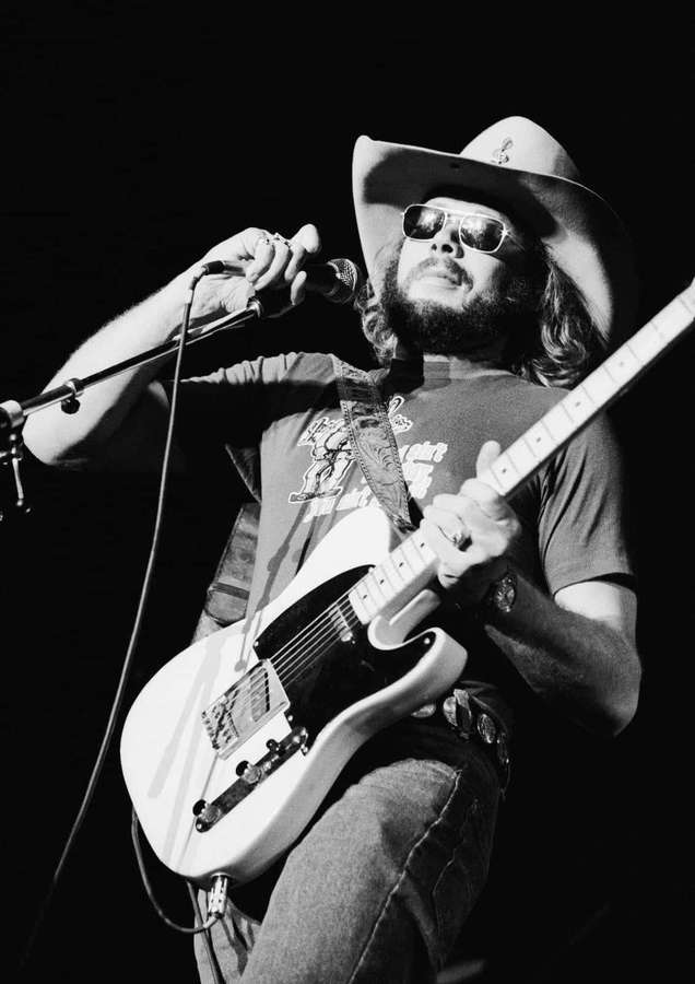 A bearded man in a cowboy hat and sunglasses plays a white electric guitar on stage. — Hank Williams Jr Wallpaper