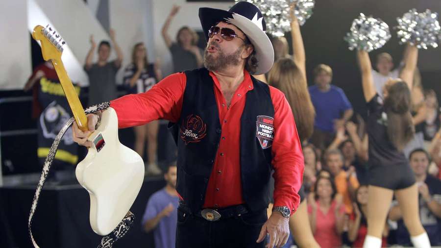 Mann mit Cowboyhut spielt weiße Gitarre auf der Bühne mit jubelnder Menge und Cheerleadern — Hank Williams Junior Wallpaper