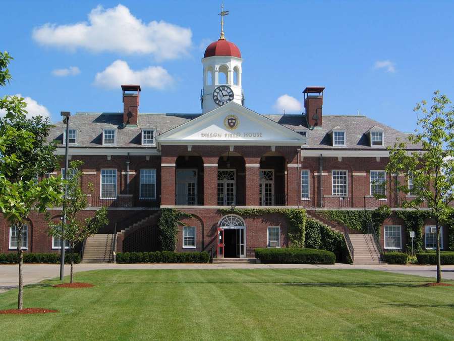 Red brick college building with clock tower and ivy-covered steps on green lawn. — Harvard University Background