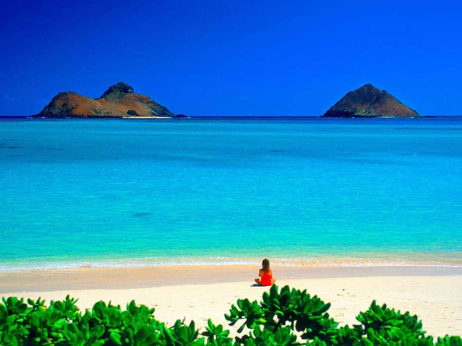 Person in orange sitting on beach facing turquoise ocean and volcanic islands. — Hawaii Beach Background