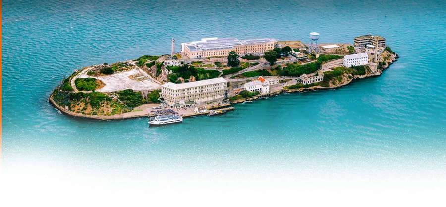 Isla de Alcatraz con edificios de la prisión y un barco turístico en aguas turquesa. — HD Agua Fondos de pantalla