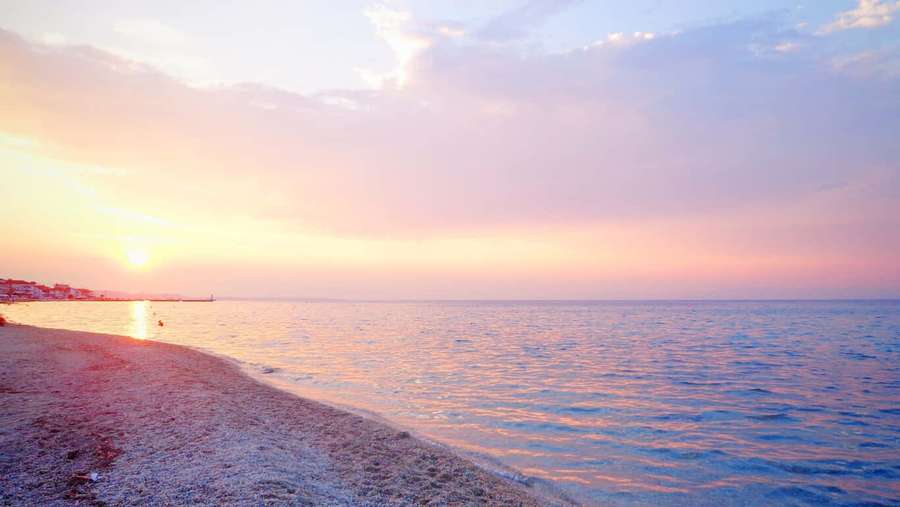 Sonnenuntergang über dem Ozean mit rosa-goldenem Himmel, der sich auf ruhigem Wasser neben einem Kieselstrand spiegelt. — HD strand Wallpaper