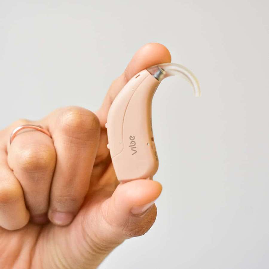 Hand holding a beige behind-the-ear hearing aid with a ring on finger. — Hearing Aid Wallpaper
