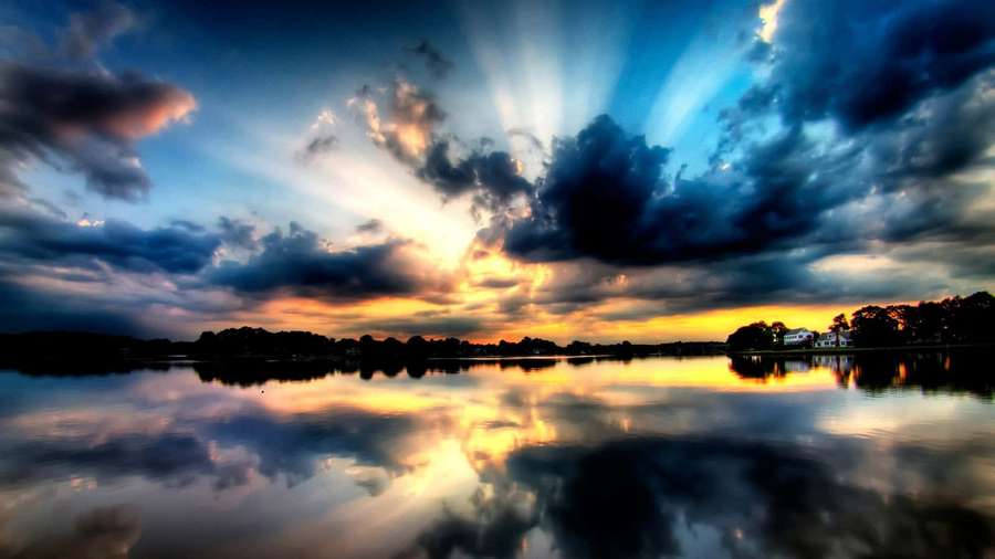 Sunset rays break through clouds over a tranquil lake with vivid reflections. — Heaven Background