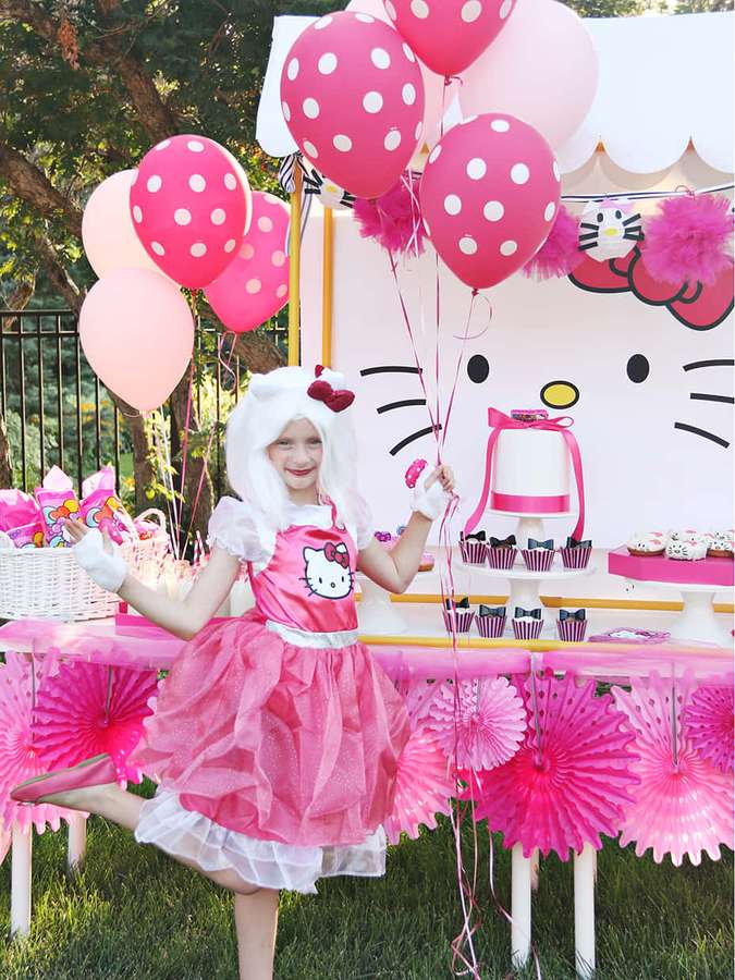 Lapsi Hello Kitty -asussa pitää ilmapalloja vaaleanpunaisissa teemajuhlissa. — Hello Kitty Juhlat Taustakuvat