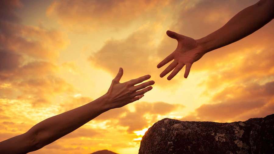 Two hands reaching toward each other against a sunset sky over a cliff. — Help Picture