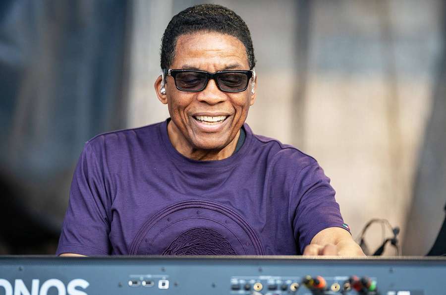 A smiling musician wearing sunglasses plays a keyboard at an outdoor concert. — Herbie Hancock Wallpaper