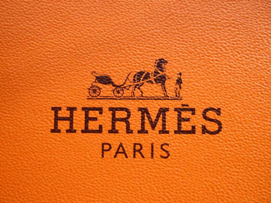 Hermès Paris-Logo auf orangefarbenem strukturiertem Leder mit Pferd- und Kutschenemblem. — Hermes Wallpaper