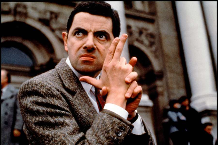 Mr Bean in einem Tweedanzug macht eine verspielte Handbewegung im Freien. — Herr Bean 4K Wallpaper
