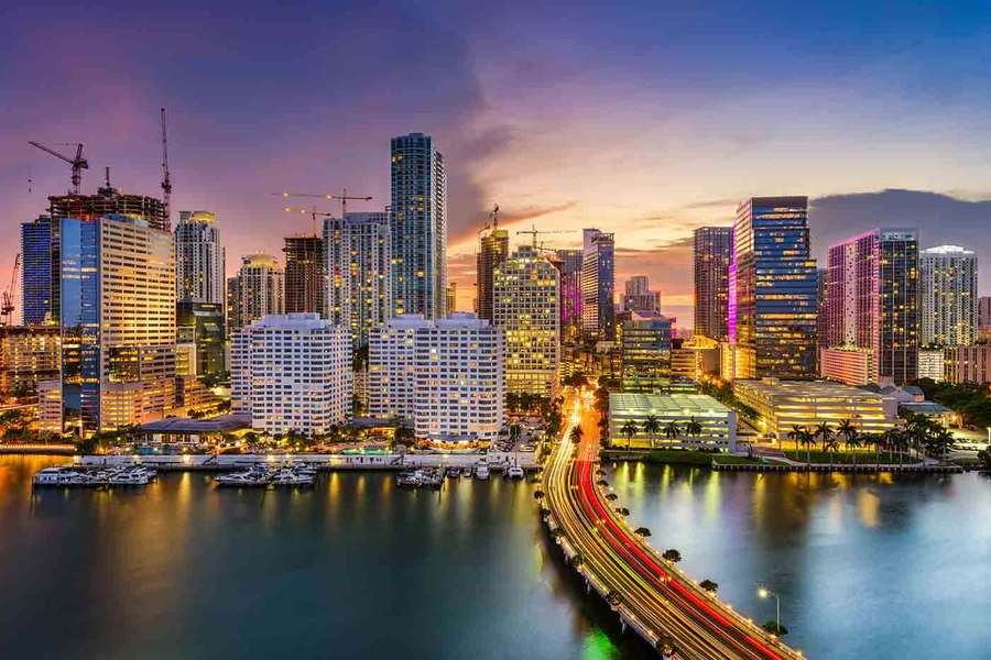 Miami cityscape at dusk with illuminated buildings and traffic lights reflecting on water. — Hialeah Wallpaper