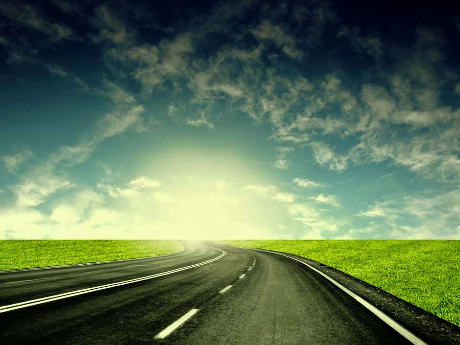 Curving road through green fields under a bright cloudy sky. — Highway Background