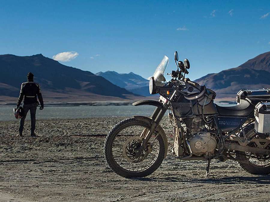 Motorcyclist standing beside adventure bike in desert with mountains — Himalayan Bike Wallpaper