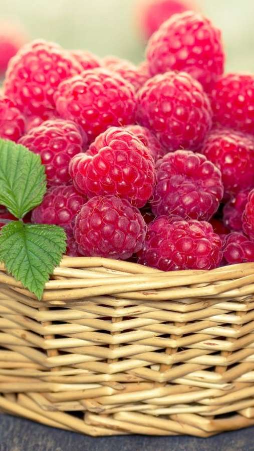 Ein geflochtener Korb gefüllt mit reifen roten Himbeeren und einem grünen Blatt. — Himbeeren Wallpaper