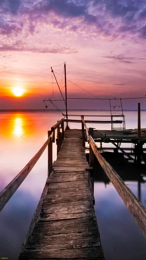 Wooden pier leading into water at sunset with colorful sky reflection — Home Screen Background