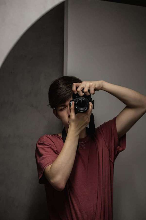 Pessoa segurando câmera contra o rosto em sala cinza minimalista. — Homem Selfie Papéis de Parede