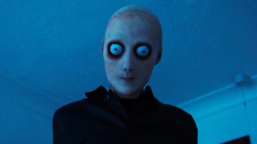 Ein kahler Alien mit leuchtend blauen Augen starrt in einem dunkelblauen Raum. — Horror Hintergrundbild