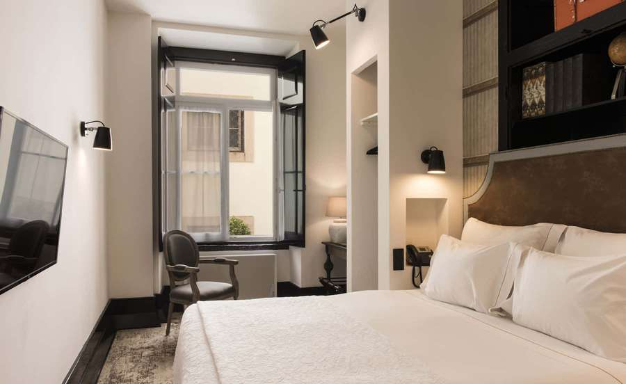 A modern hotel room with a bed, chair, and window with warm lighting. — Hotel Room Wallpaper