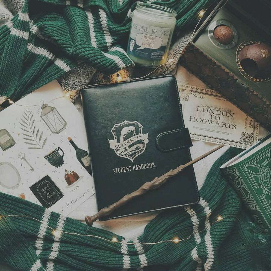 Slytherin themed items including scarf handbook wand and candle arranged on a flat surface. — Hp Aesthetic Wallpaper