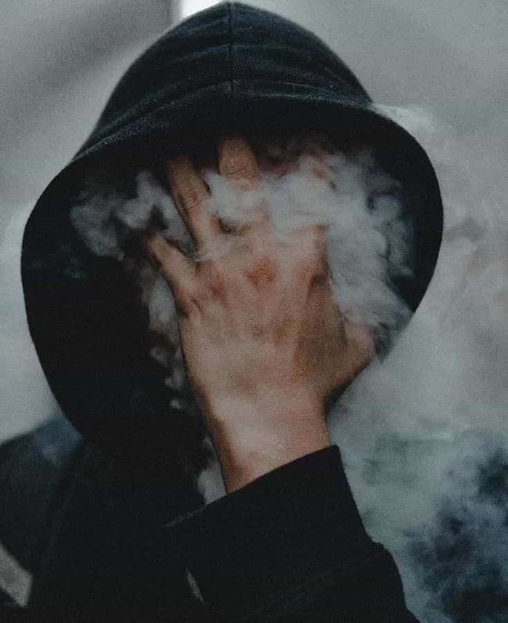 Persona con sudadera oscura cubriéndose la cara con la mano mientras vapor blanco gira a su alrededor. — Humo HD Fondos de pantalla
