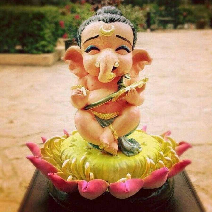 Una estatua colorida del bebé Ganesha tocando una flauta sobre una flor de loto. — Imagen Fondos de pantalla