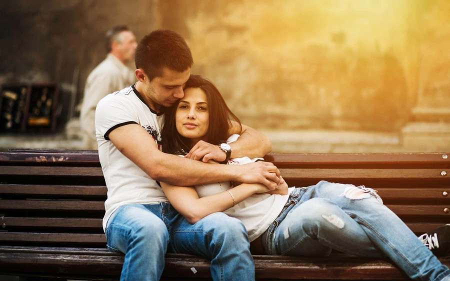 Una pareja se acurruca en un banco del parque bajo la luz dorada del sol. — Imágenes de Cuddleando Imágenes