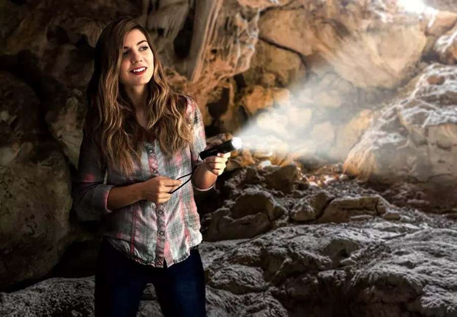 Mujer sosteniendo una linterna dentro de una cueva rocosa sonriendo a la cámara — Imágenes de linterna Imágenes
