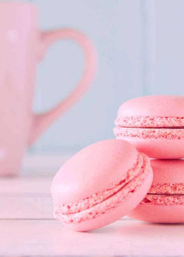 Macarons rosas y una taza sobre una mesa de madera con fondo pastel suave. — Imágenes de Macarons Imágenes