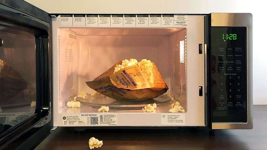 Bolsa de palomitas explotando en un microondas con granos derramándose. — Imágenes de microondas Imágenes