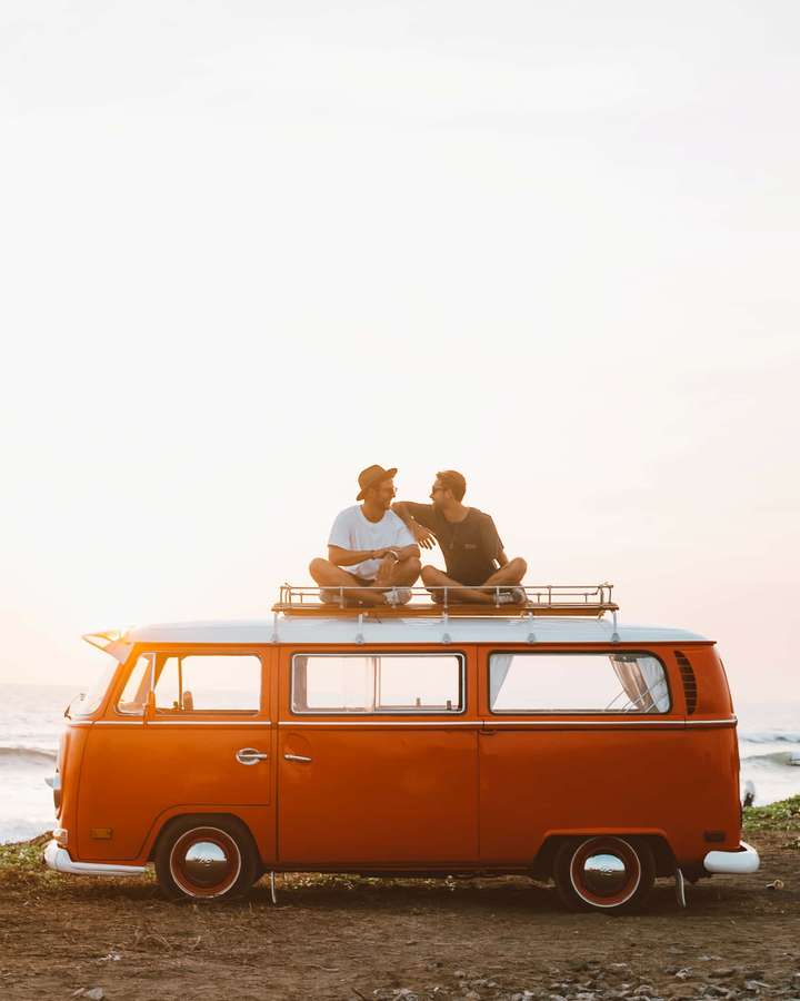 Duas pessoas sentadas em uma van laranja vintage ao pôr do sol à beira do oceano. — Imagens de van Fotos