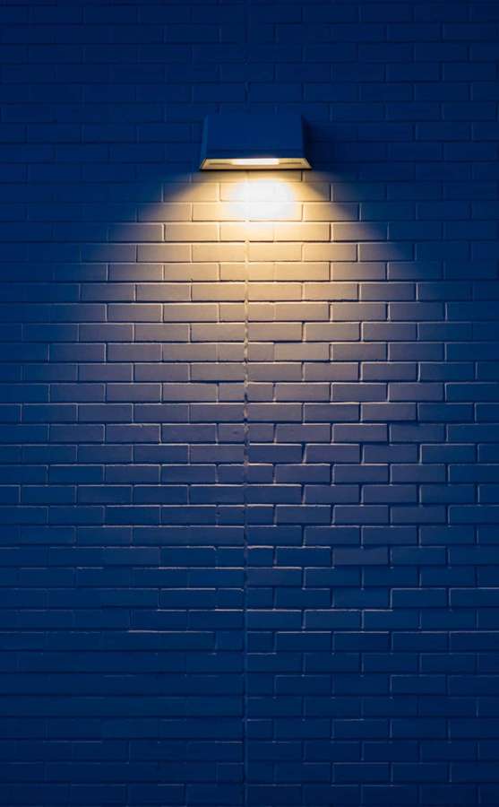Un singolo apparecchio di illuminazione illumina un muro di mattoni blu di notte. — Immagini creative Sfondi
