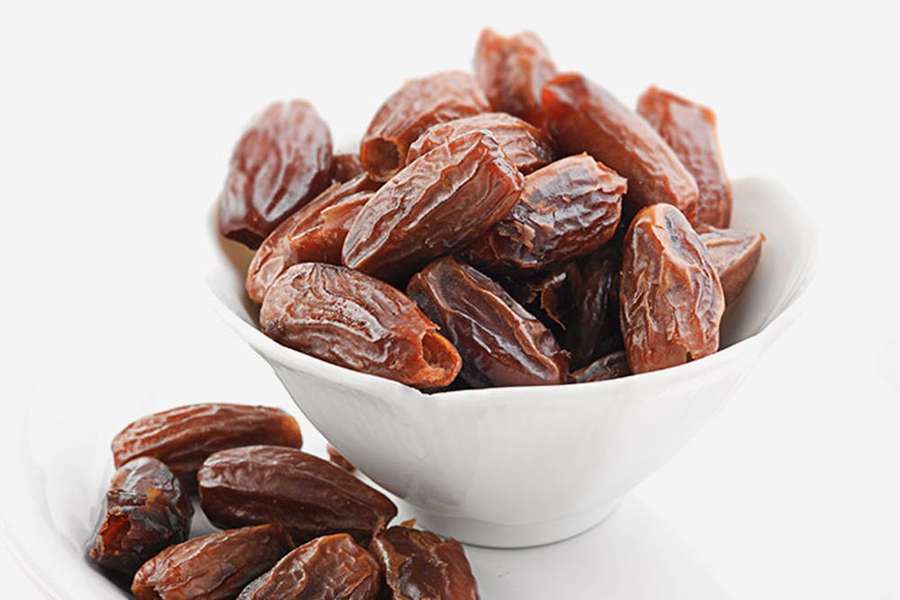Una ciotola bianca piena di datteri marroni carnosi con alcuni sparsi accanto. — Immagini di date Sfondi