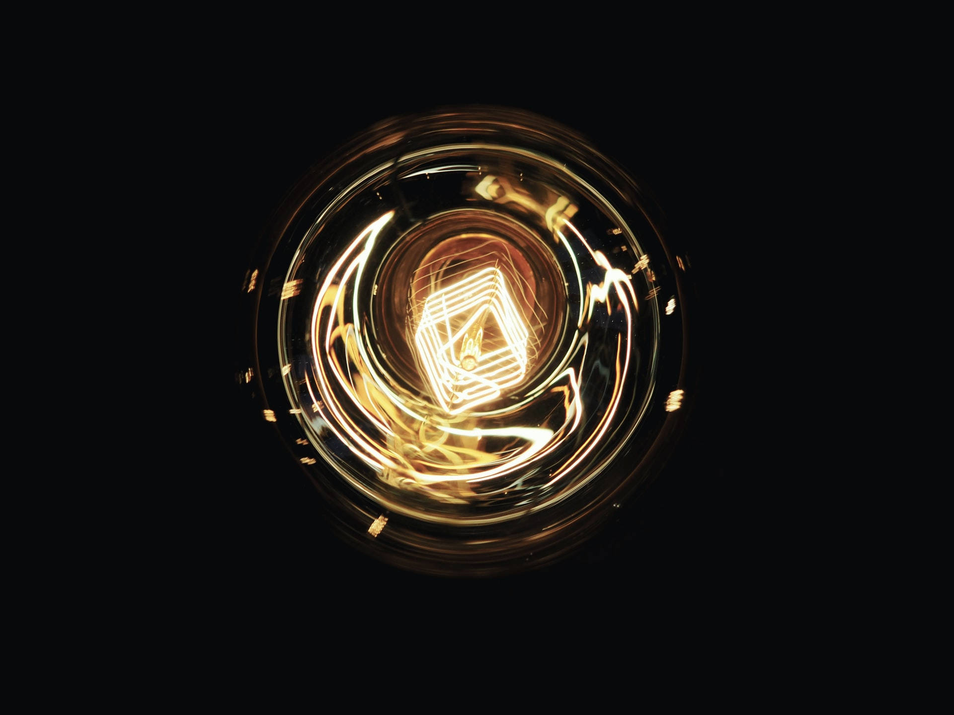 Close-up of a glowing filament bulb with swirling light trails on black background — Imperative Background