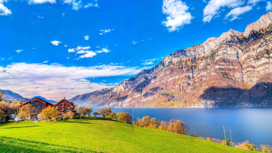 Chalet rojo en colina cubierta de hierba junto al lago con montañas de fondo — Impresionante HD Fondos de pantalla