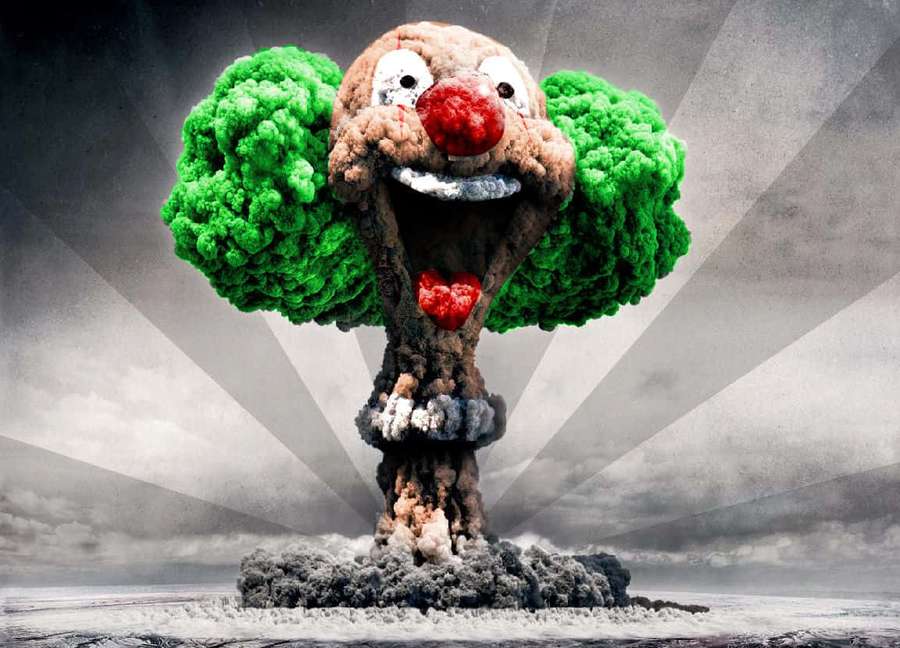 A clown-faced nuclear explosion with green smoke hair and red nose against a stormy sky. — Inane Wallpaper