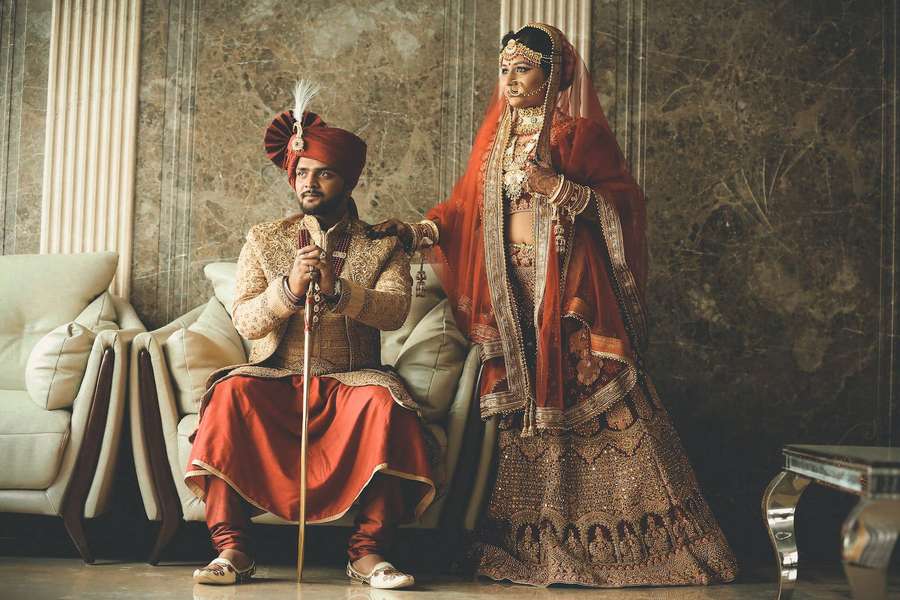 Indian wedding couple in traditional red and gold attire posing indoors. — Indian Wedding Wallpaper