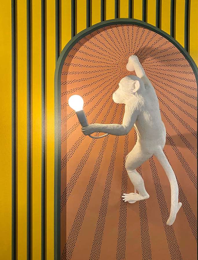 White monkey sculpture holding a lit bulb in an arched doorway with yellow stripes. — Interesting Background