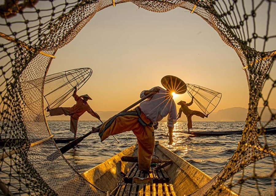 Silhouetted fishermen casting nets from wooden boats at golden sunset. — Interesting Picture