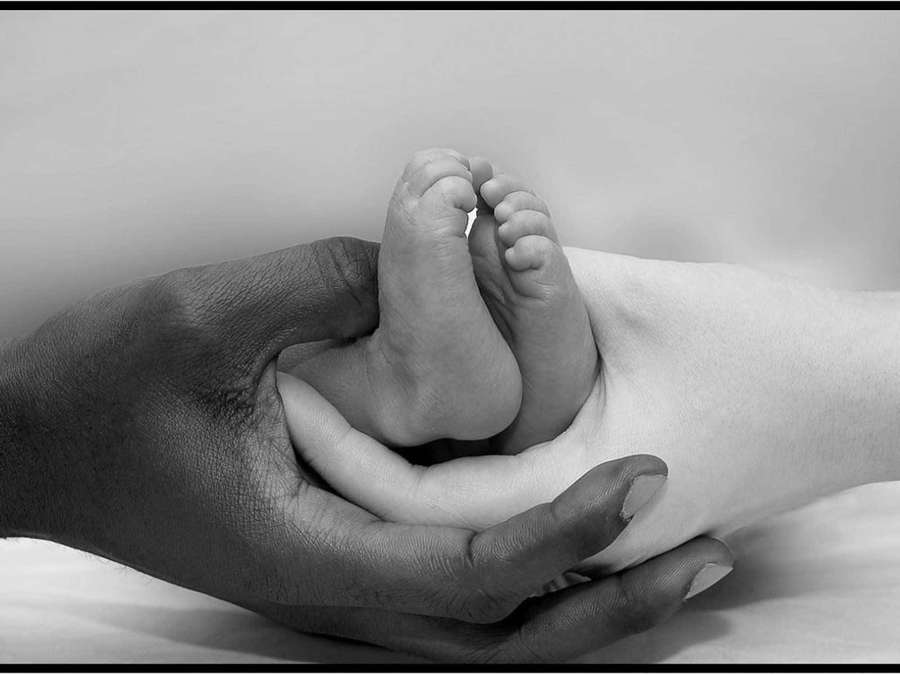An adult hand gently holding a baby's feet in a tender moment. — Interracial Wallpaper