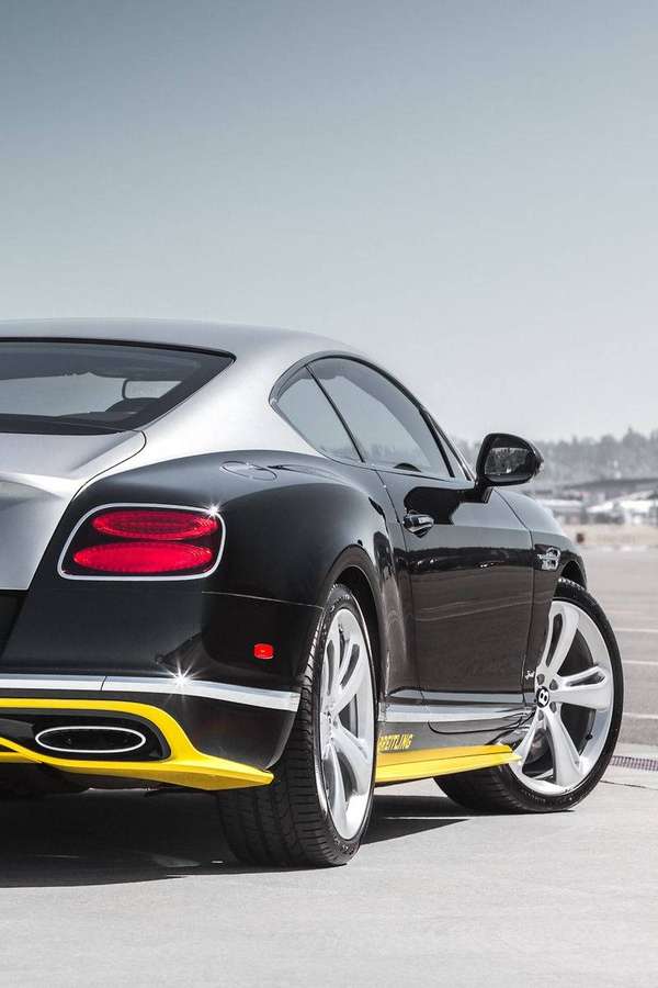 Carro esportivo Bentley preto com acentos amarelos estacionado no asfalto sob sol forte. — iPhone Bentley Papéis de Parede