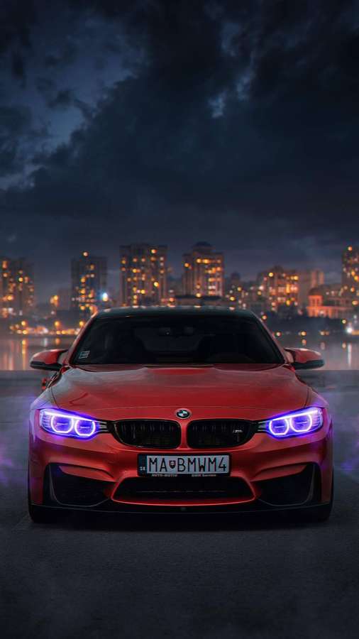 Red BMW sports car with blue headlights parked at night in a city with lit buildings. — iPhone Car Background