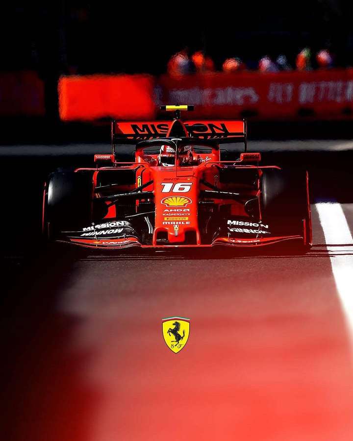Carro vermelho da Ferrari F1 correndo à noite em uma pista com logotipos de patrocinadores e uma multidão ao fundo. — iPhone Ferrari Papéis de Parede