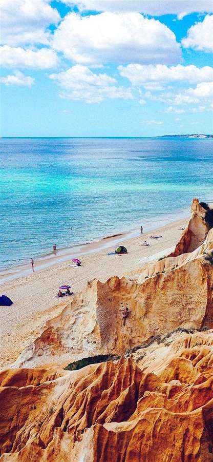 Golden cliffs overlook a turquoise beach with people enjoying the sunny day. — iPhone X Beach Background