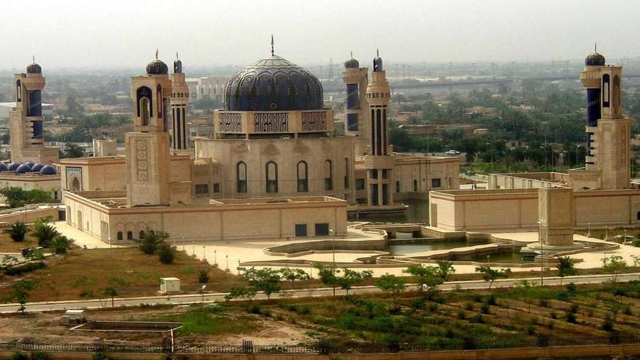 Grand mosque with blue dome and minarets overlooking cityscape. — Iraq Background