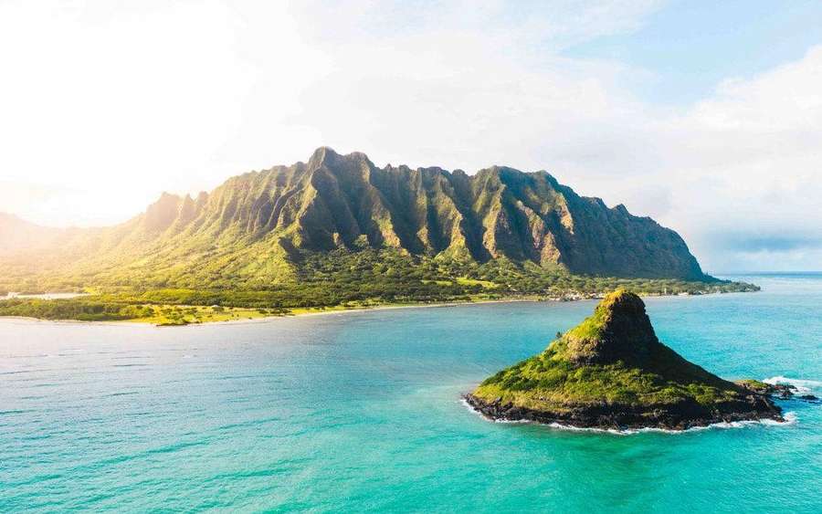 Exuberantes montañas verdes se elevan desde las aguas turquesa del océano con una pequeña isla cercana. — Islas Fondos de pantalla